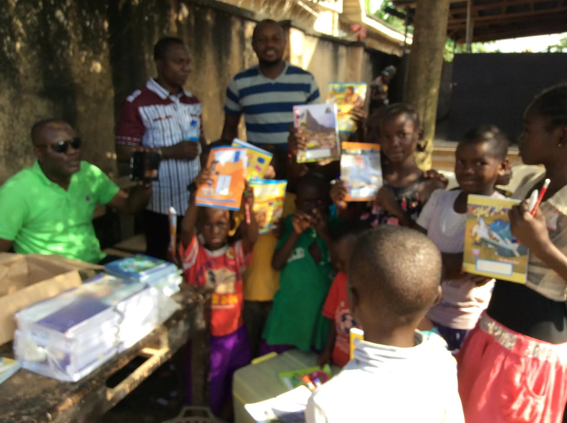 Children hold up new exercise books and learning materials given to them by RAMES Empowerment Foundation.