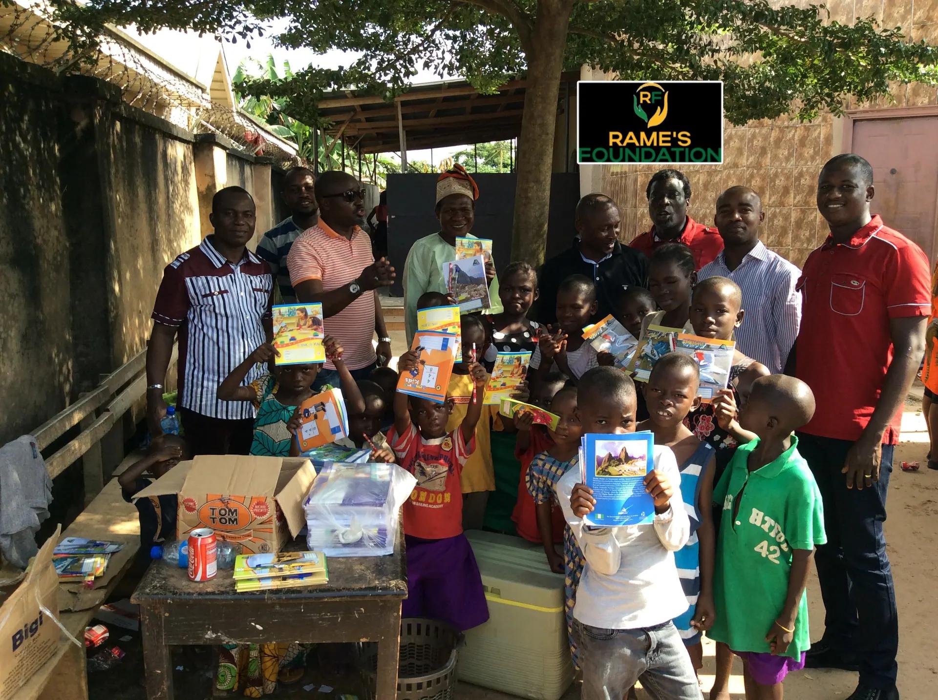 A group of smiling children raise their new exercise books beside RAMES Empowerment Foundation volunteers.