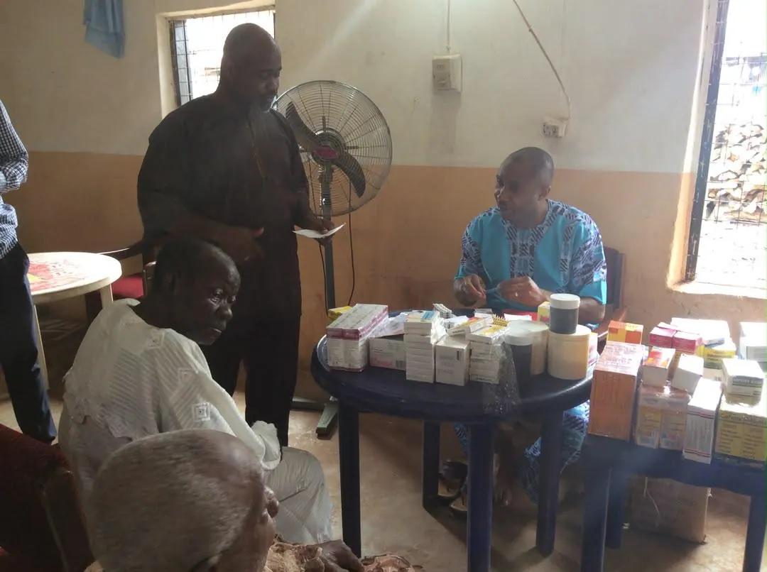 A team member addresses seated residents while medicines are dispensed at a nearby table.