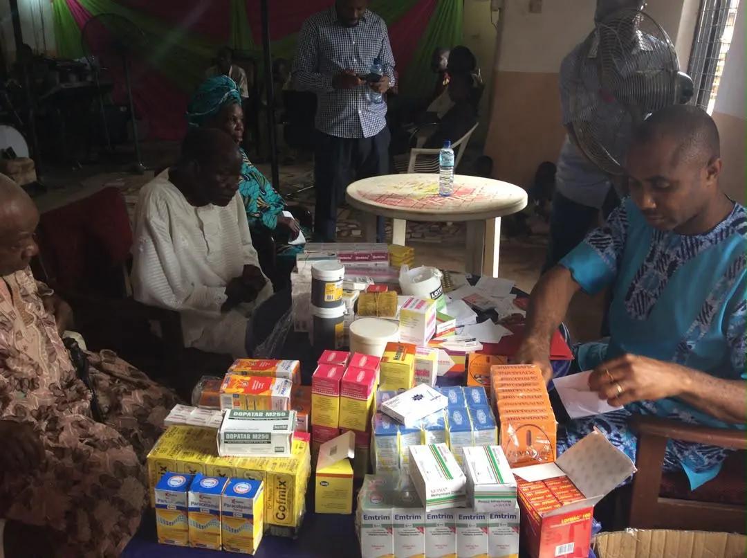 A volunteer dispenses medicines at a table while an elderly woman is attended to.