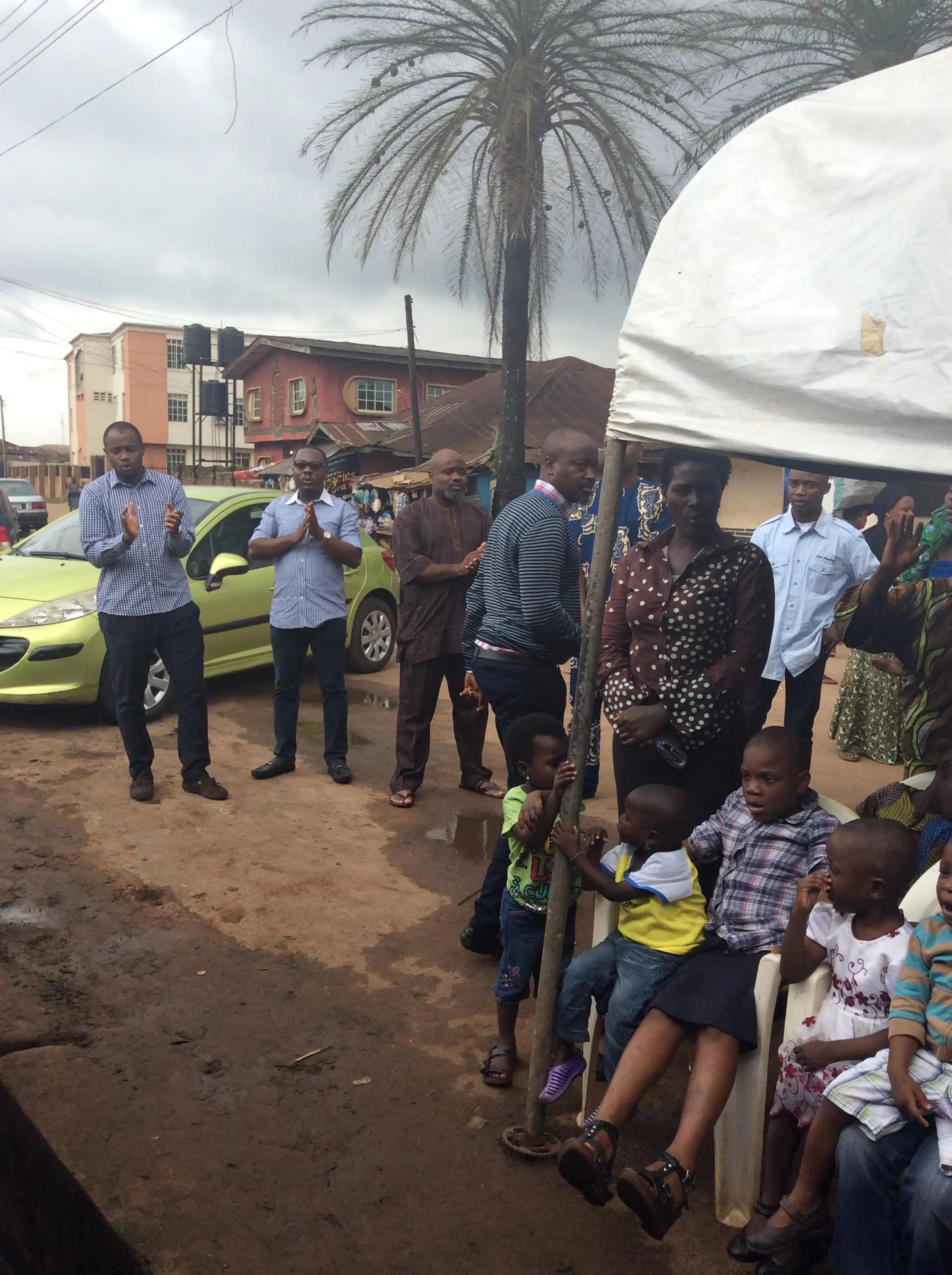 Residents including children gather outdoors beside a canopy for a community outreach.