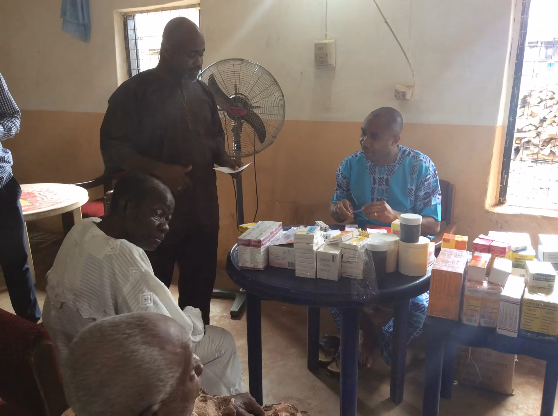 Volunteers sort medicines at a table while elderly community members wait to be attended to.