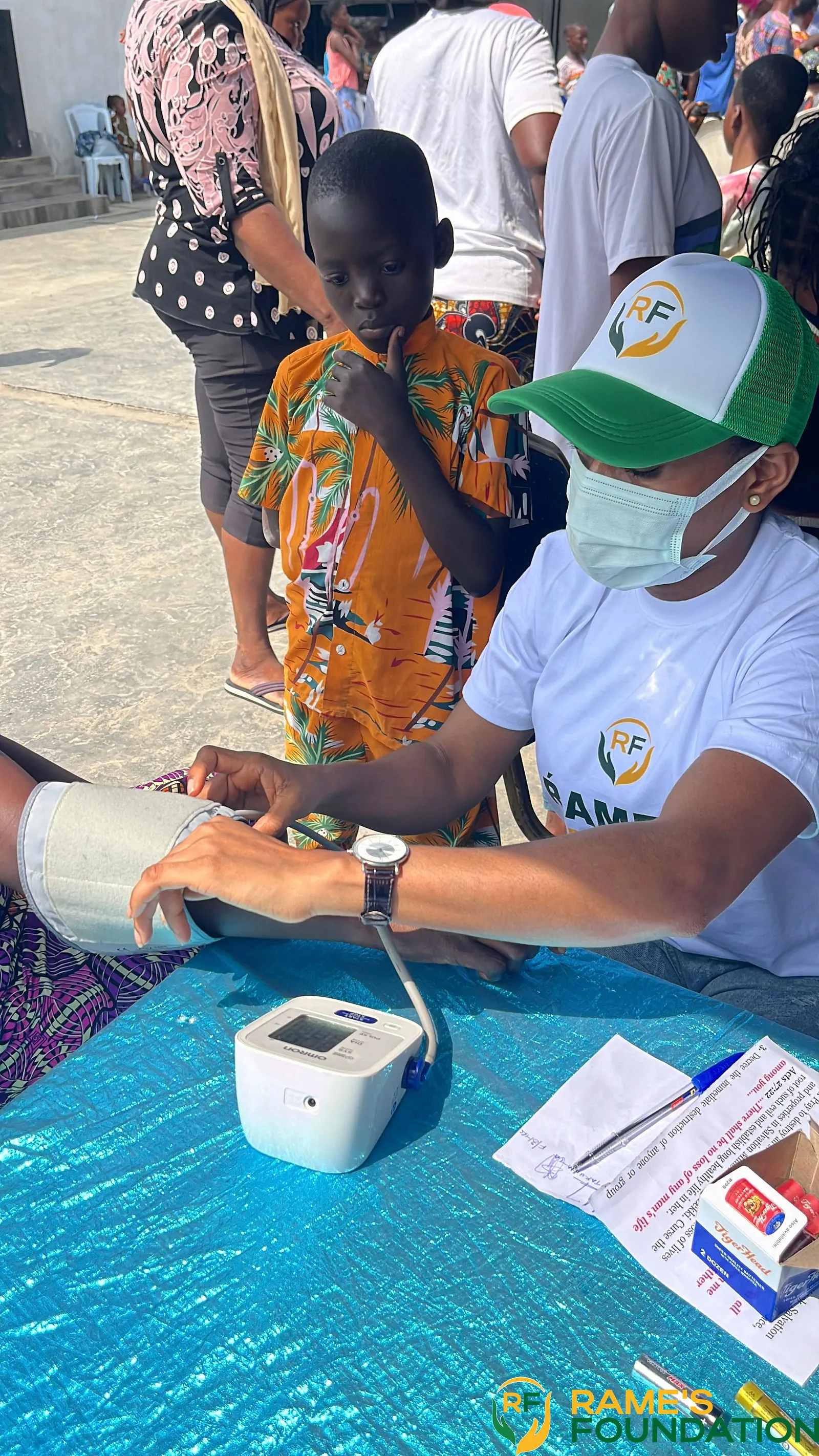 A RAMES volunteer takes a woman's blood pressure with a digital monitor at a blue outreach table.