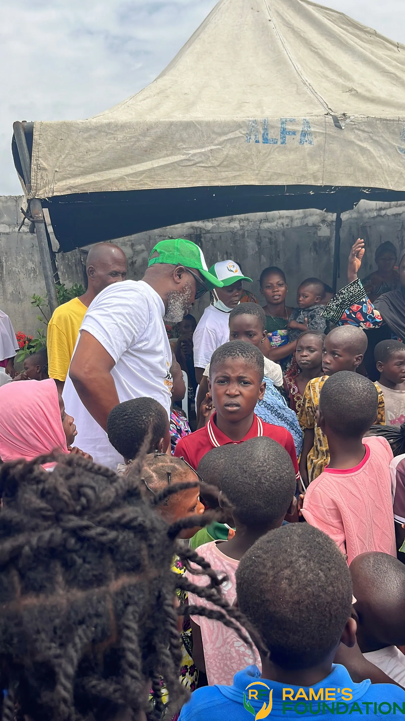 Children gathered under a tent look up at a volunteer during a community outreach.