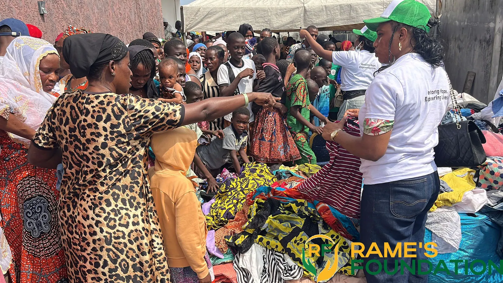 A volunteer holds up a garment for women choosing clothing from a table of donated items.
