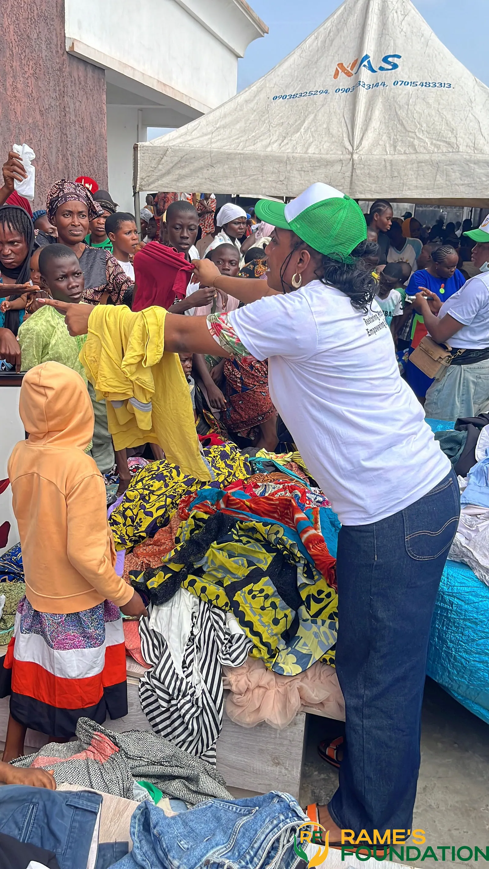 A volunteer holds up a garment among a crowd of residents under a tent at a clothing distribution.