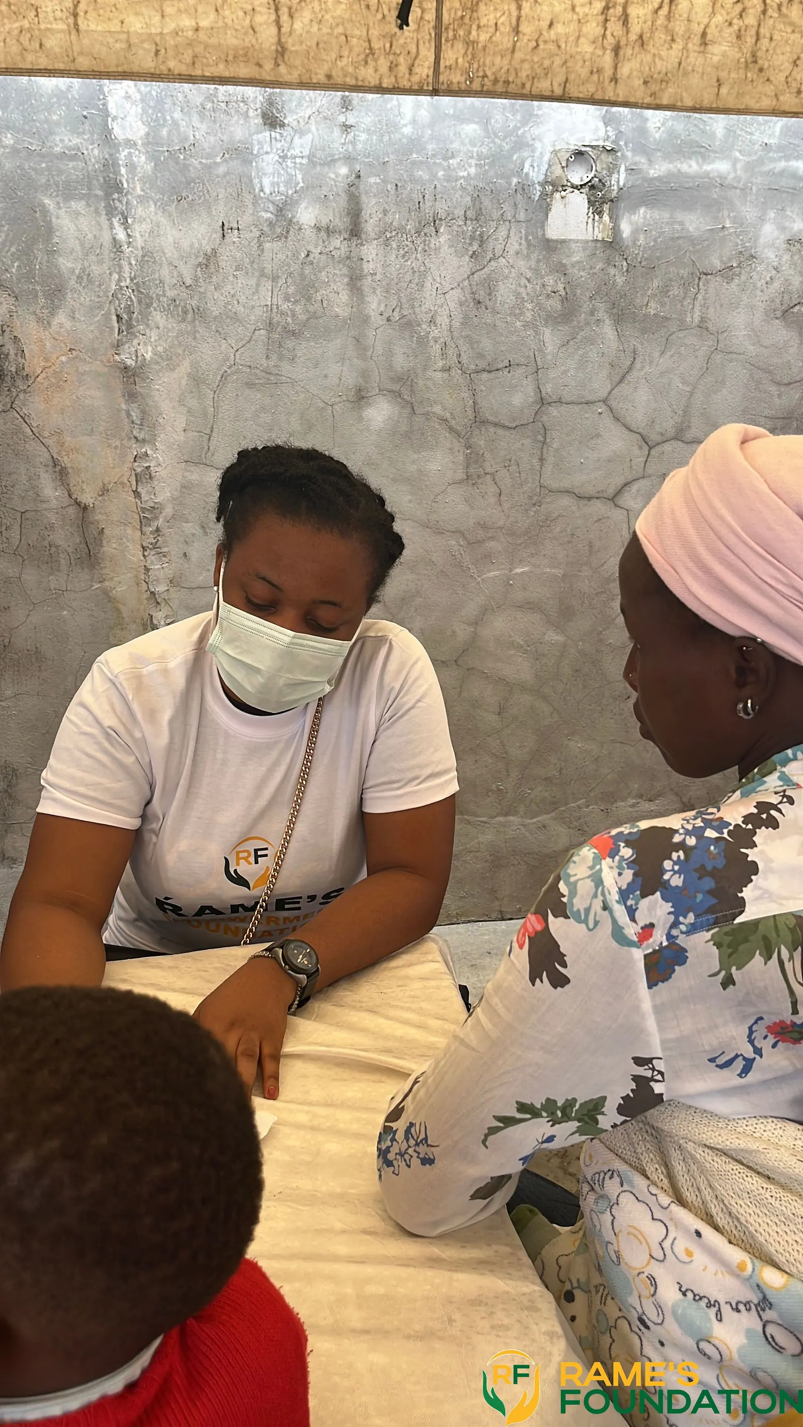 A masked RAMES volunteer sits at a table consulting with a woman during a medical outreach.