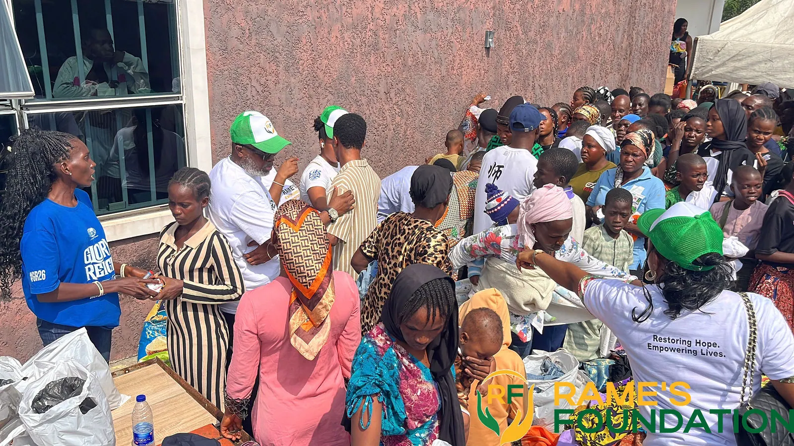 Volunteers hand items to a dense crowd of residents lined up along a wall at a community outreach.