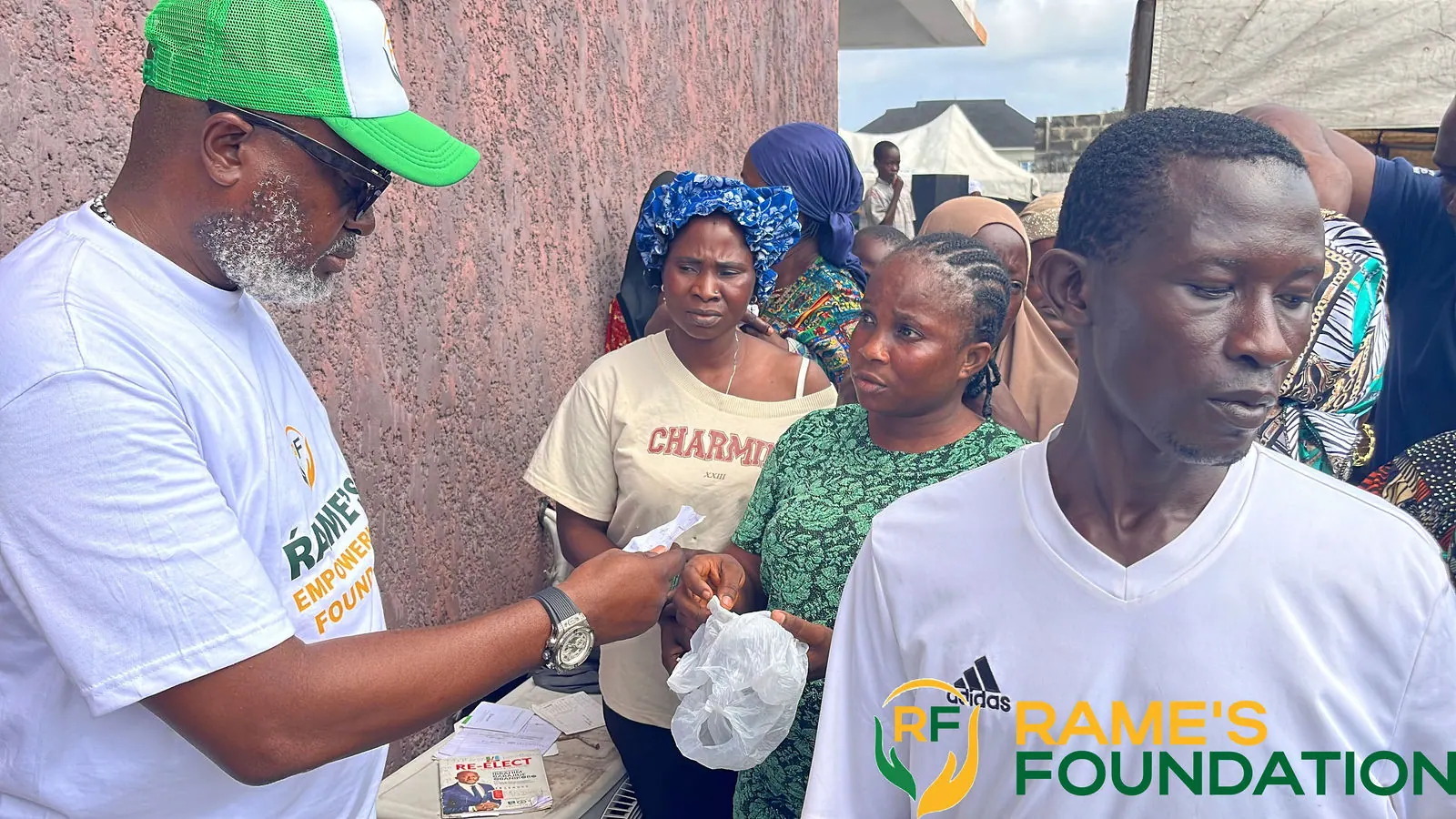 A RAMES volunteer hands a small pack to a man in a crowd of residents.