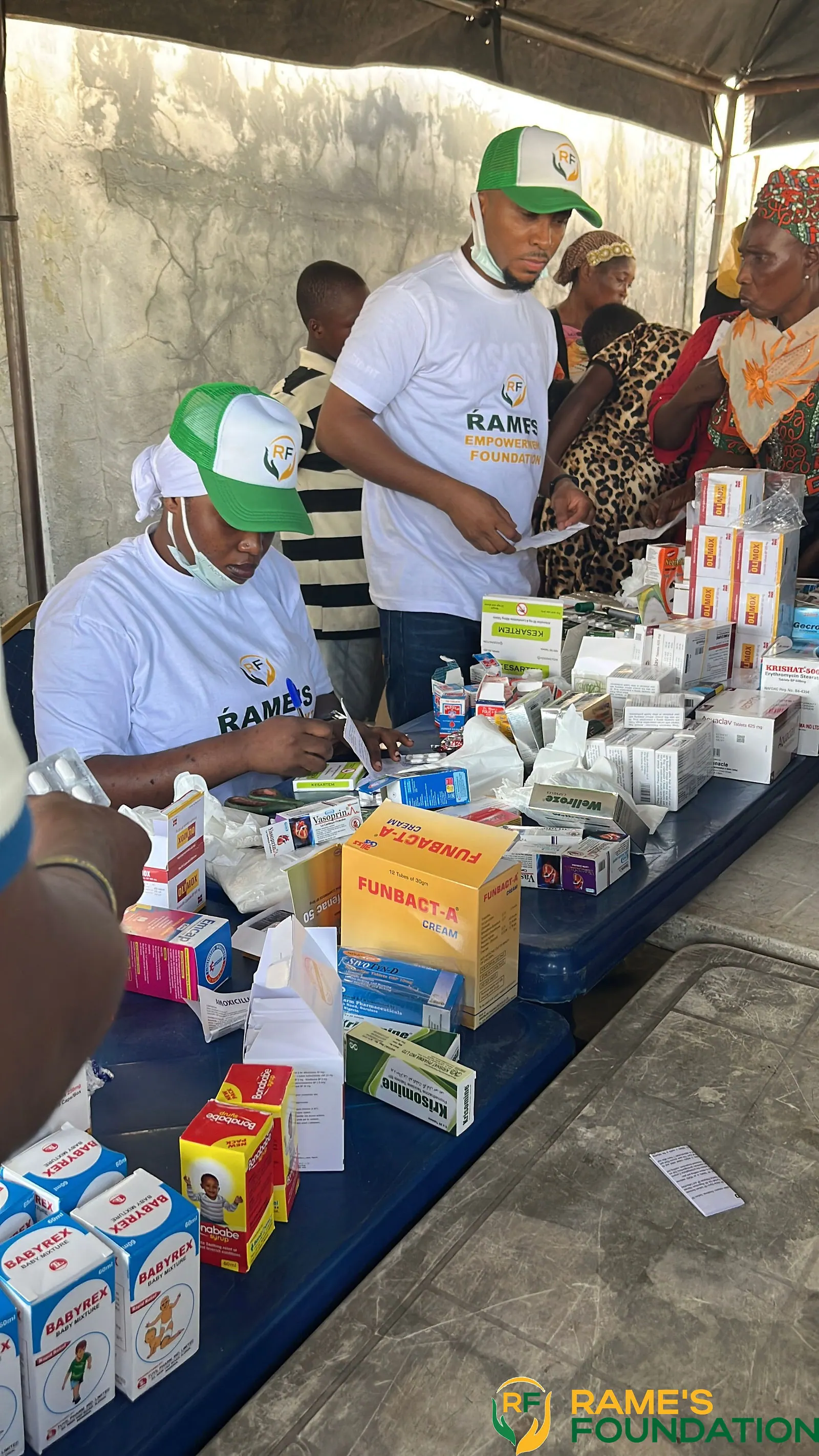 RAMES volunteers stand behind a table covered with boxes of medicines and supplements at an outreach.