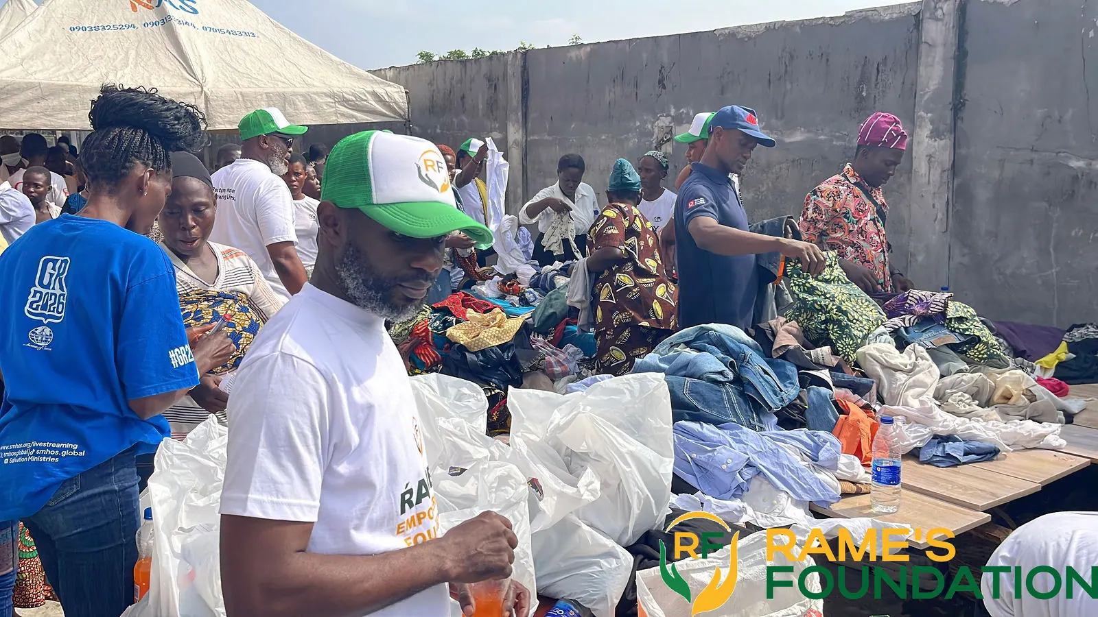 Volunteers in RAMES caps pack and hand out bags of relief items beside a table of clothing.