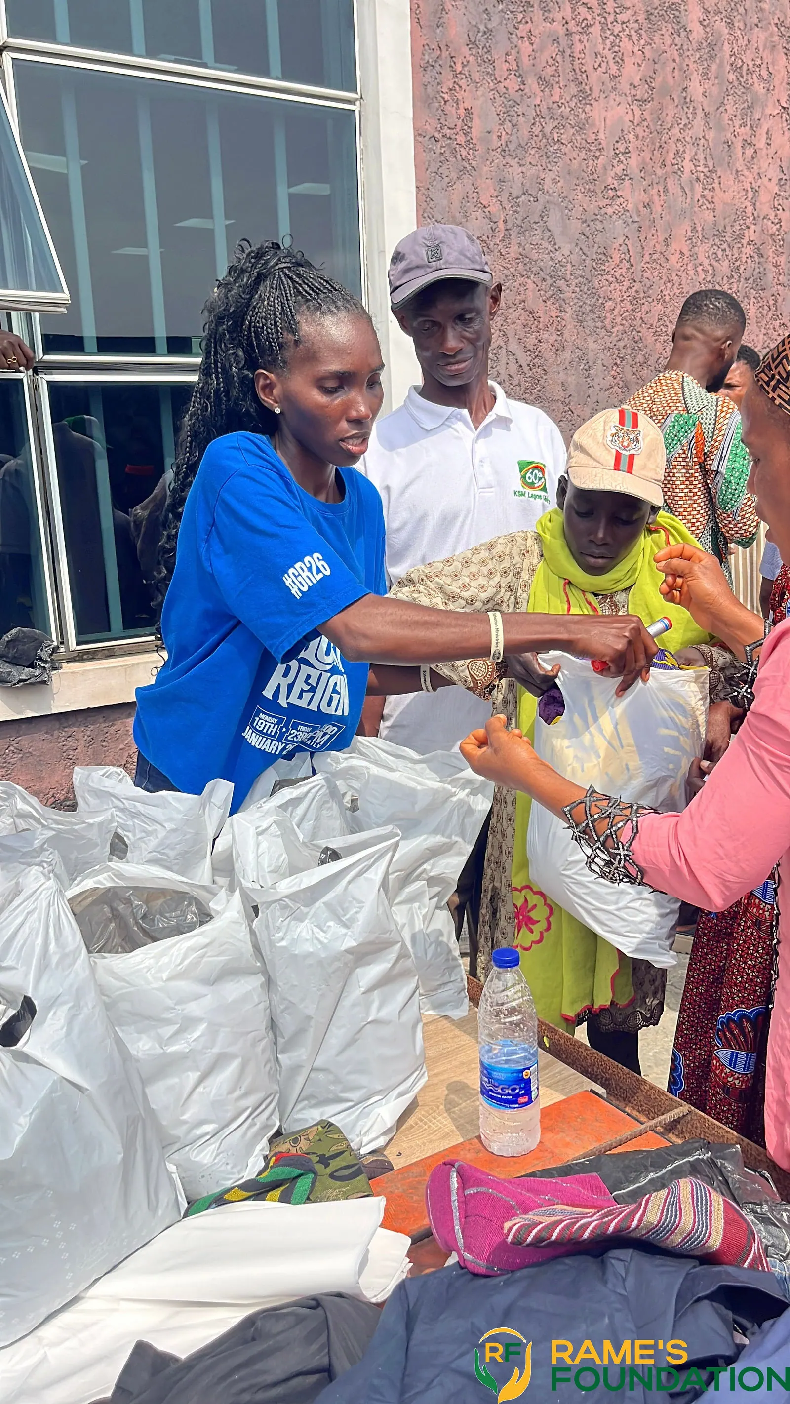 A volunteer in blue hands bags of relief items to residents waiting in a queue.