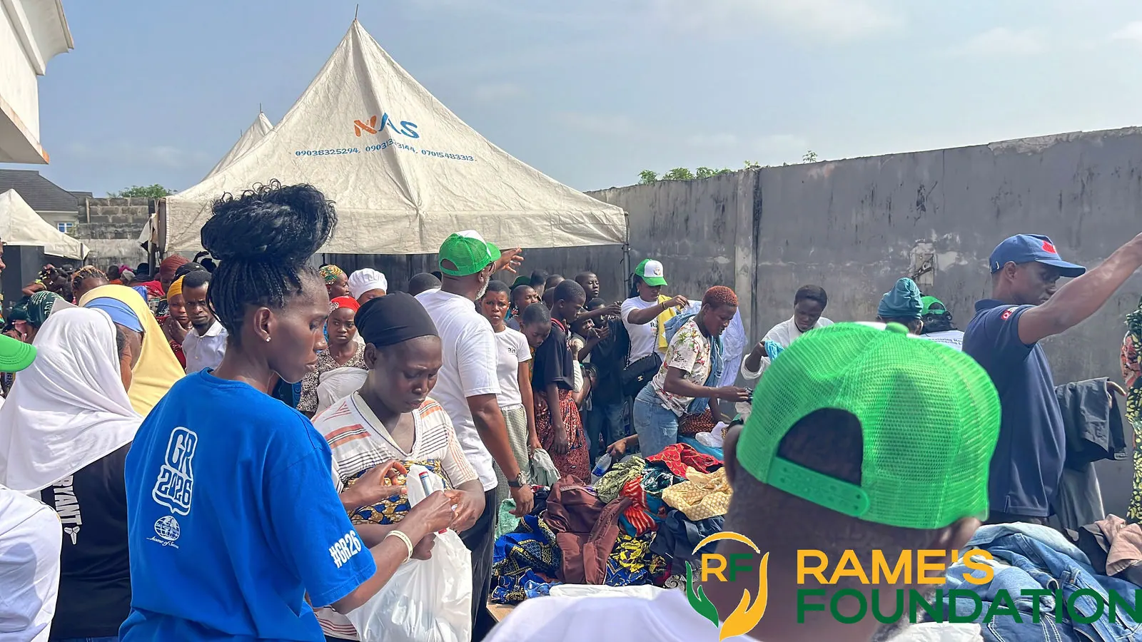 Volunteers under a white tent hand out relief items to residents queuing in the sunshine.