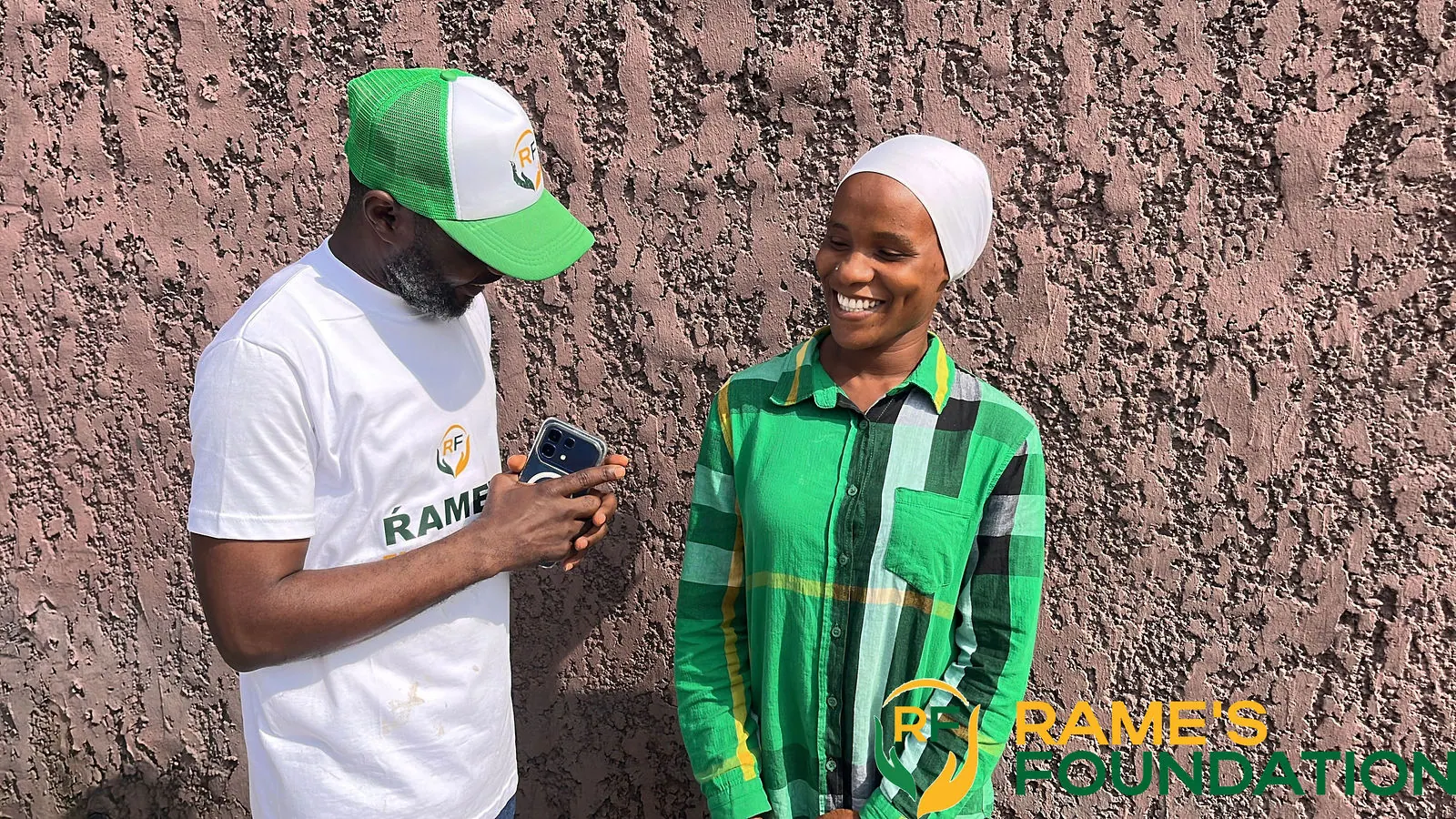 A RAMES volunteer in a cap chats with a smiling young woman in a green checked shirt.