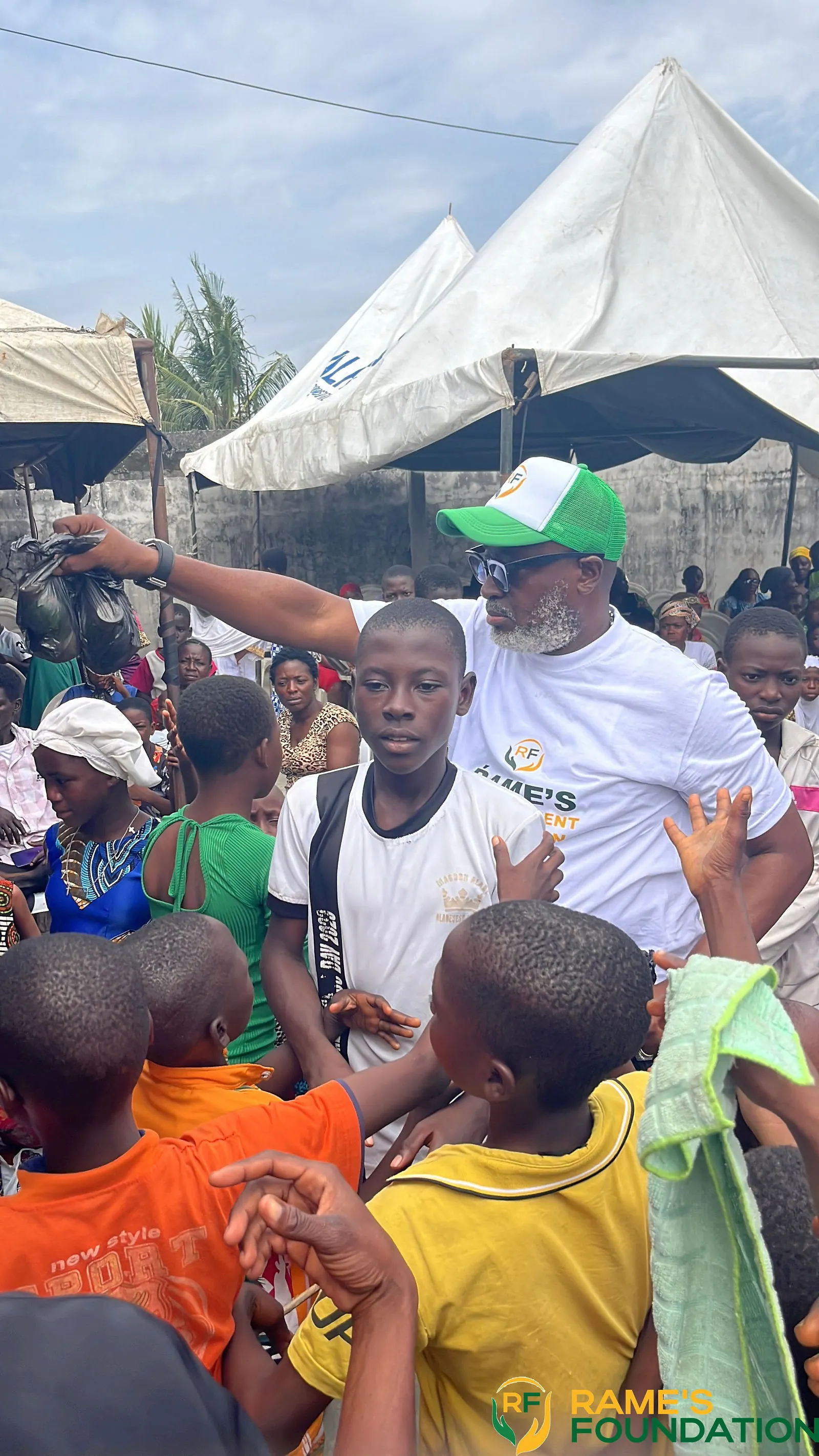 A volunteer gestures towards a boy in a crowd of children under the outreach tents.