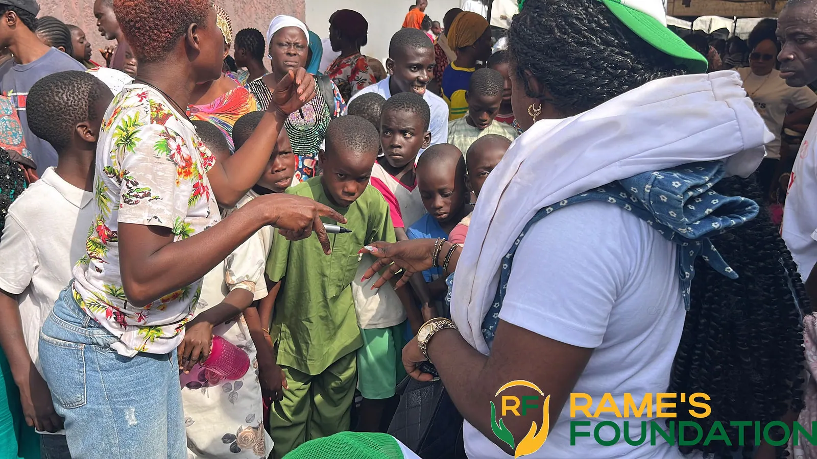 A RAMES volunteer is surrounded by children and residents at a busy community outreach.