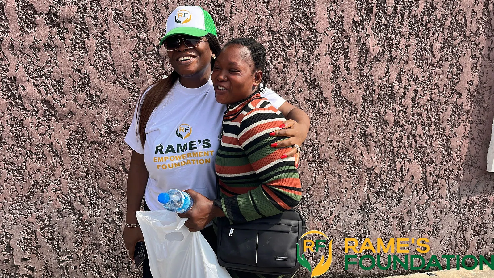 A RAMES volunteer hugs a smiling woman who is holding a bag of items she received.