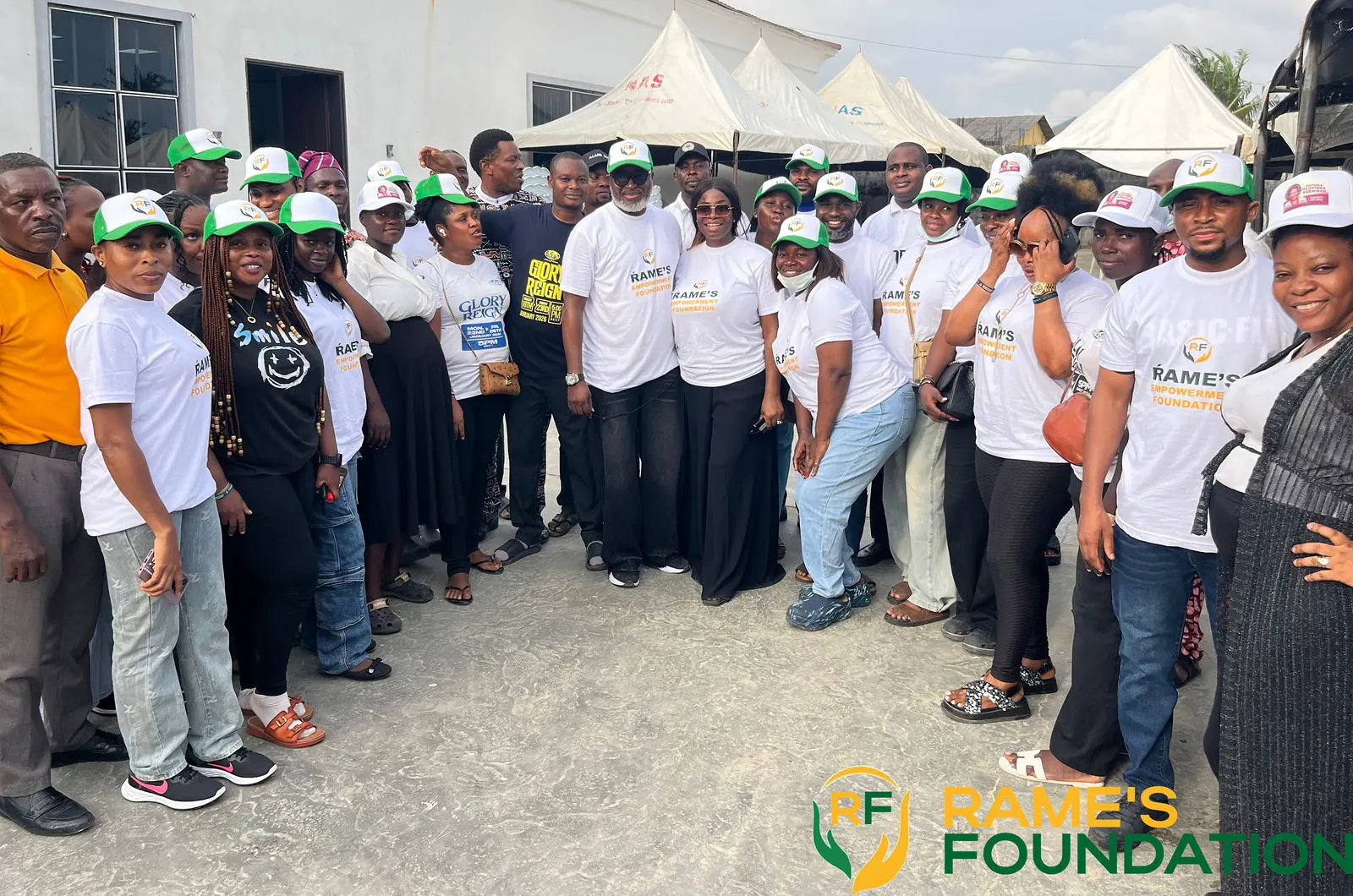 A large group of RAMES Empowerment Foundation volunteers in white branded T-shirts and green caps.