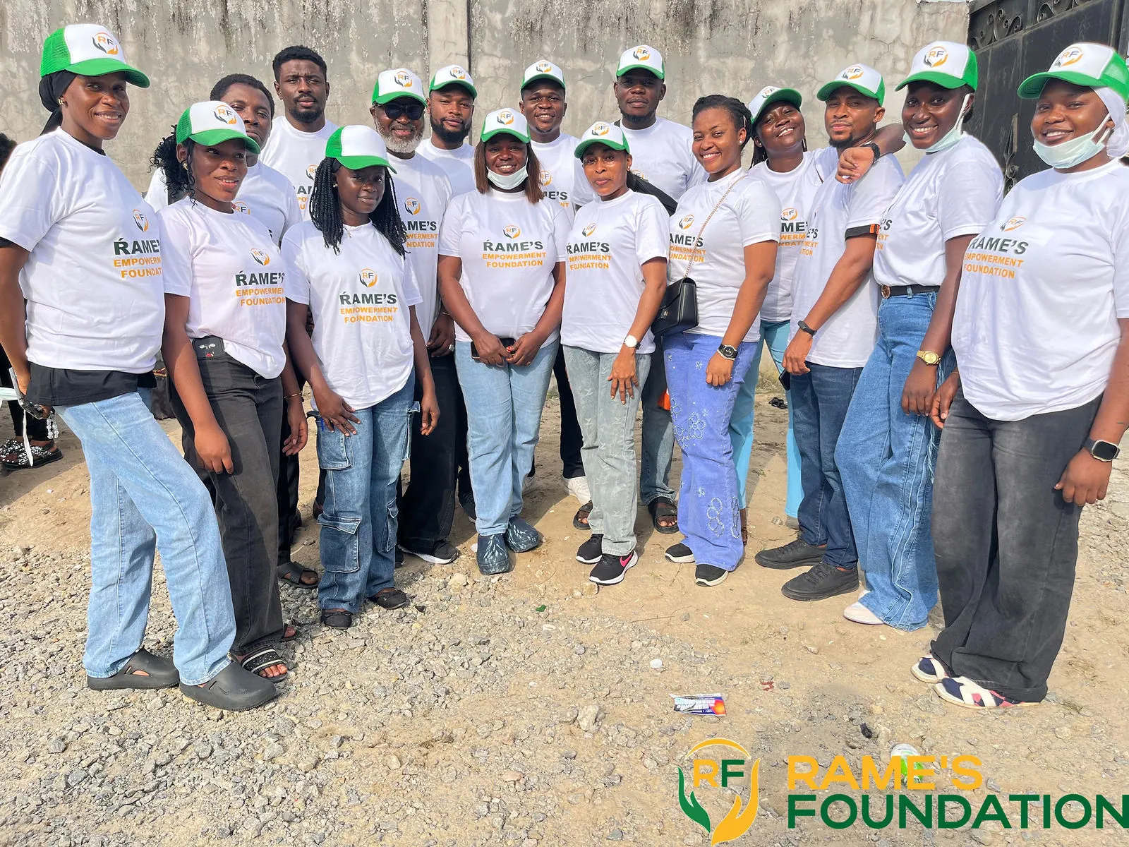 A row of RAMES volunteers in white T-shirts and green caps standing together outdoors.