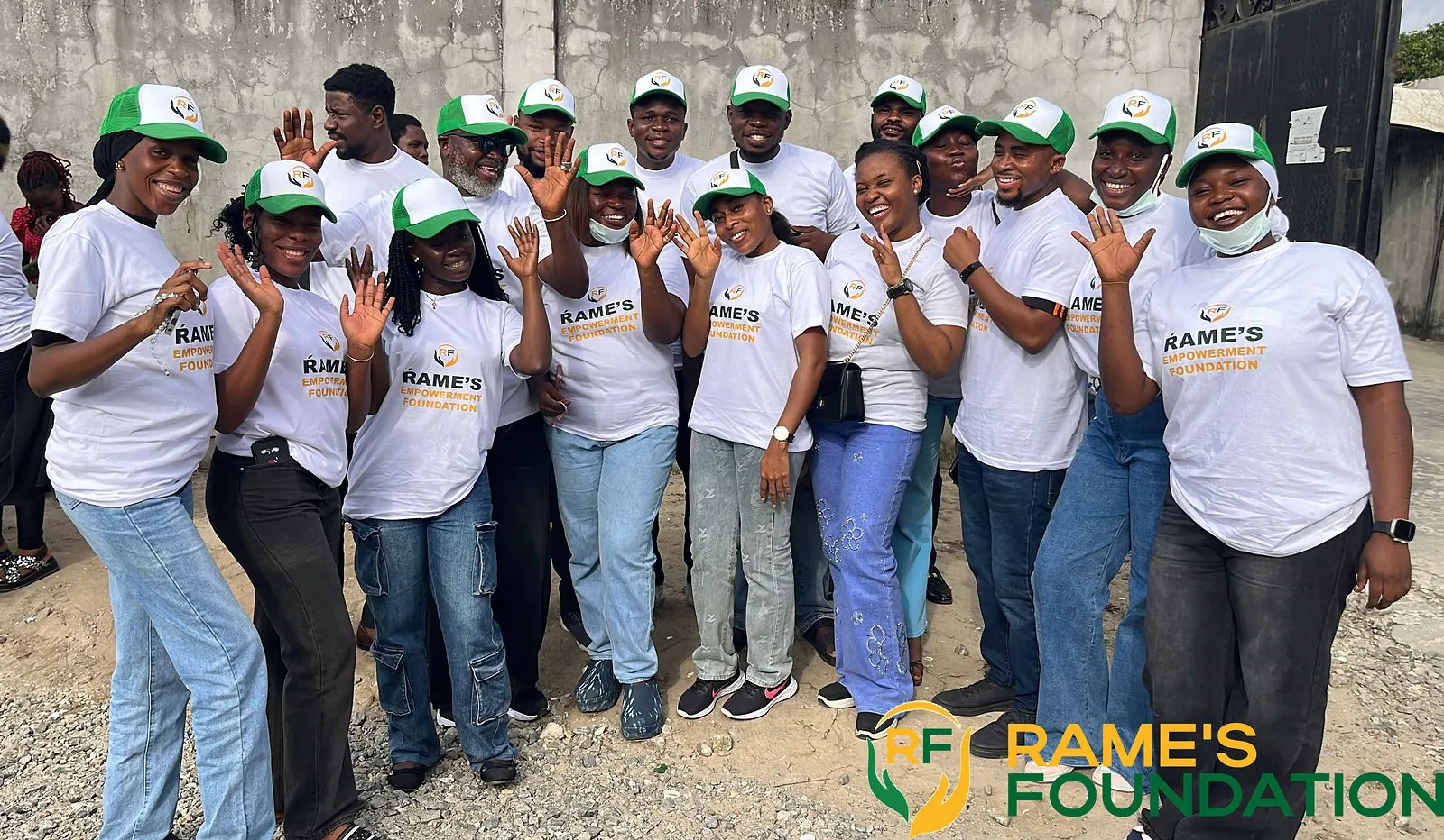 RAMES volunteers in white T-shirts and green caps wave and cheer together.