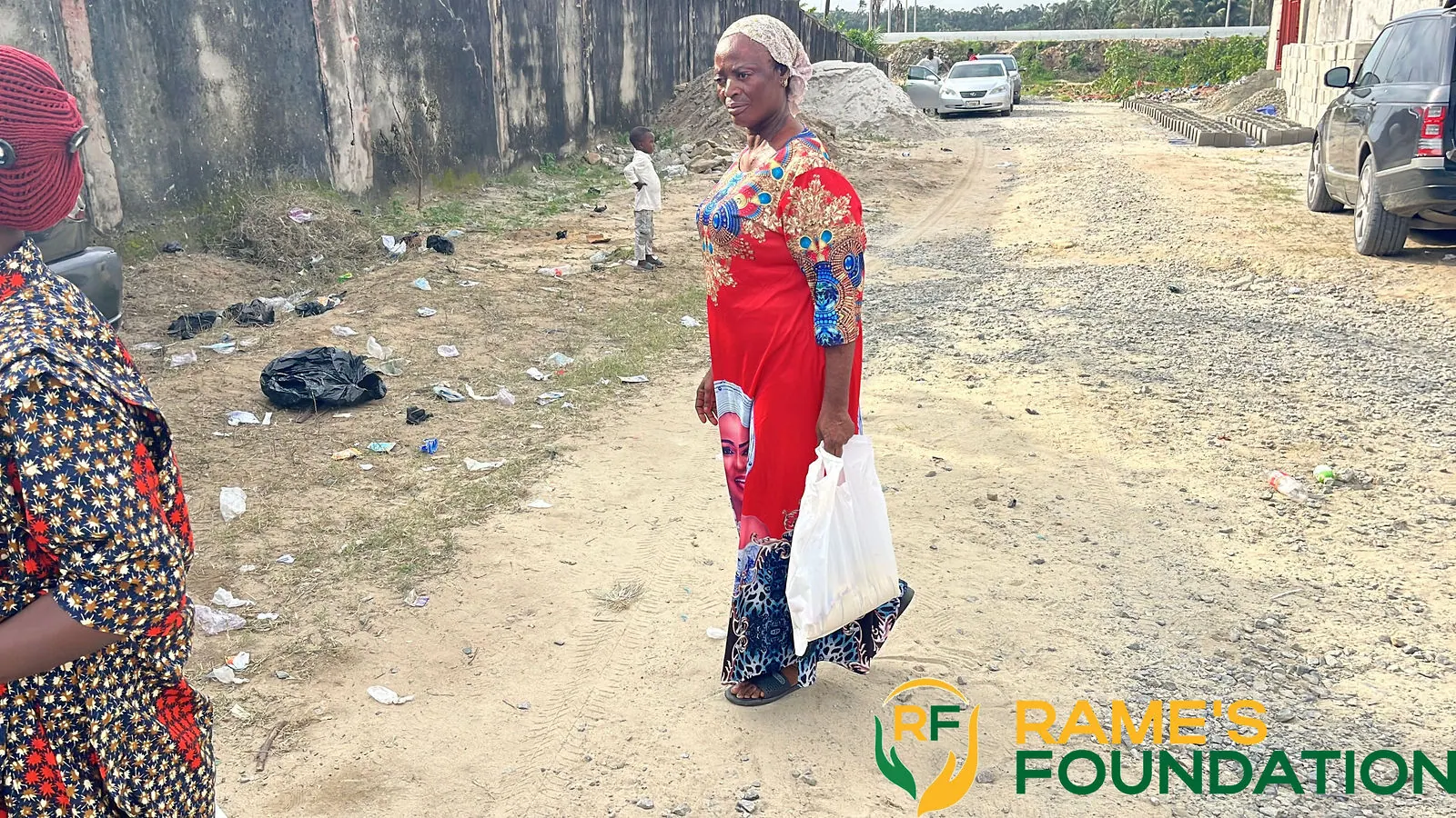 A woman in a red dress walks away from the outreach carrying a bag of relief items.